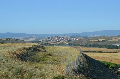 Paisaje con vista de un pueblo en la distancia y ruinas romanas en primer plano.