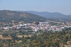 View of a hillside village with a church in the center and mountains in the background.