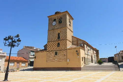Kirche mit Turm und Uhr in Lucillos, Toledo, bei blauem Himmel.
