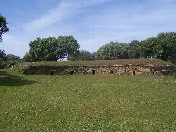 Stone structure in a green field with trees and blue sky.