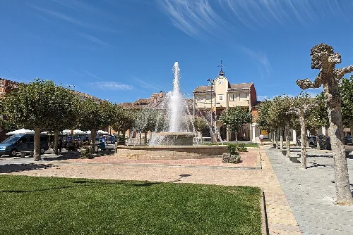 Square with fountain, trees, and buildings in Villada, Palencia.