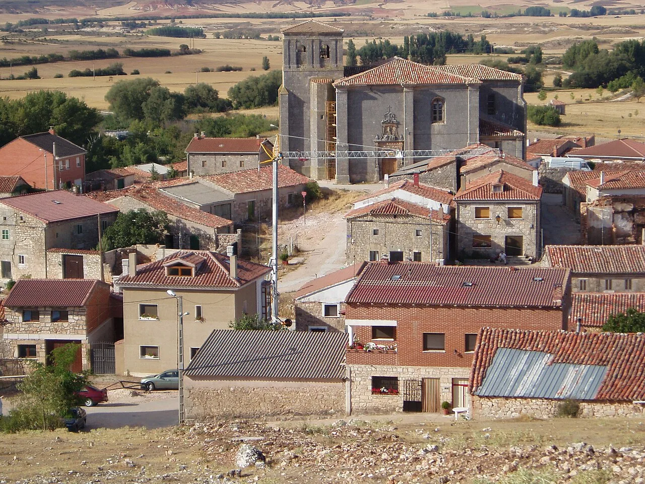 Häuser und eine Kirche in einem Dorf mit Feldern im Hintergrund.