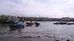 Barcos en el puerto de Luanco con cielo nublado.