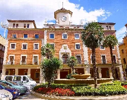 Rathausgebäude mit Uhr, Palmen und Brunnen auf dem Platz.