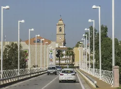 Street with cars, lampposts, and a church in the background in Carlet