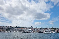 Hafen von Sada mit Booten und Gebäuden, bewölkter Himmel.
