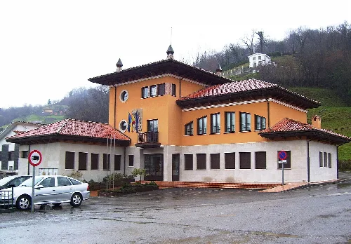 Edificio del ayuntamiento de Bimenes con varias ventanas y un tejado rojo.