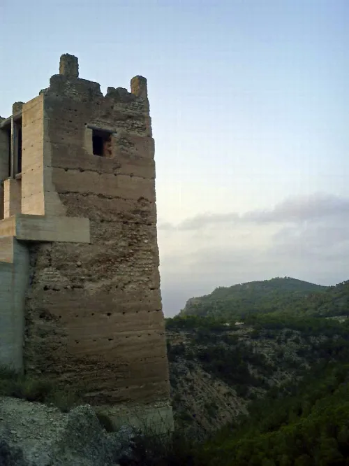 Steinerner Burgturm in Pliego mit grünen Hügeln im Hintergrund.