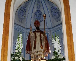 Estatua de San Agustín en un altar con flores blancas.