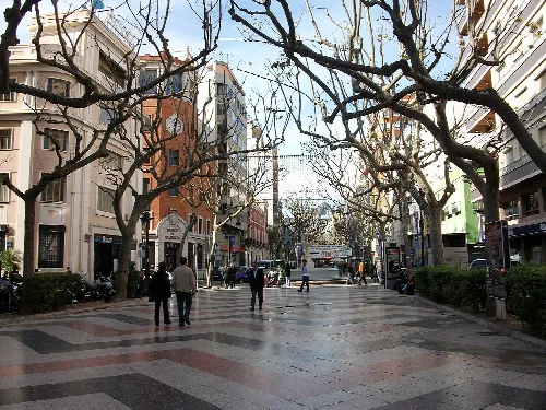 A pedestrian street with leafless trees and people walking in Gandia.