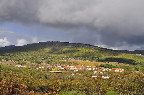 Blick auf ein Dorf umgeben von Natur mit bewölktem Himmel und Herbstlichtern.