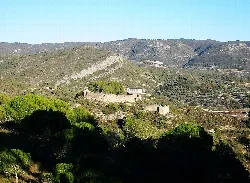 Burg auf Hügeln mit Steinmauern und umliegender Vegetation.