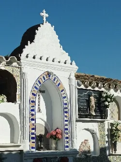 Panteón blanco con detalles azules y una cruz en la parte superior.