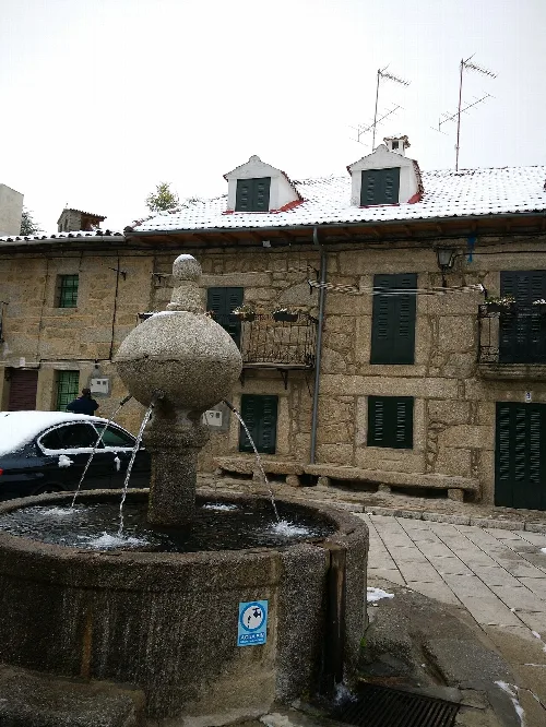 Steinbrunnen auf dem Hauptplatz mit Steingebäuden und schneebedeckten Dächern.