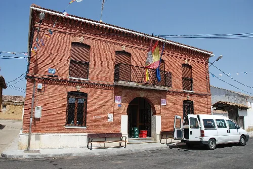 Red brick town hall with windows and a flag in Ayuela.