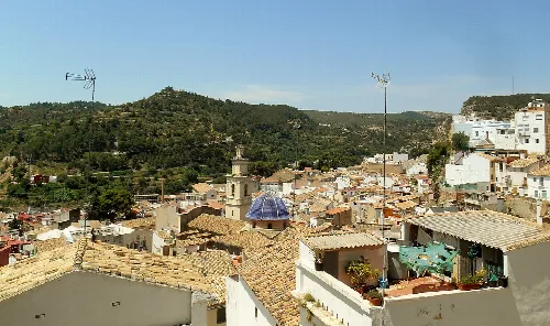 Panoramablick auf die Burg und Häuser von Buñol mit grünen Hügeln im Hintergrund.