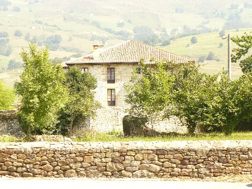 Casa de piedra con árboles y colinas verdes en el fondo.