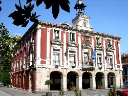 Edificio del ayuntamiento de Mieres con banderas y reloj en la torre.