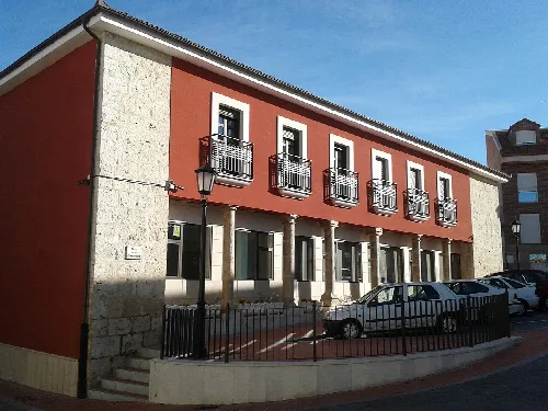 Edificio con columnas en la fachada trasera, balcones y coches en la calle.