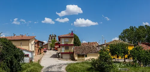 Häuser und Straße in Cubilla, Soria, mit Bäumen und blauem Himmel mit Wolken.