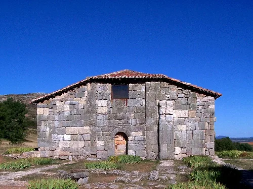 Small stone church with red-tiled roof under a blue sky.