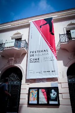 Festivalplakat mit Bein- und Filmband-Design hängt an einem Gebäude in Málaga.