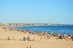Weitblick auf den Strand mit vielen Sonnenschirmen und Menschen am Sand und Meer.