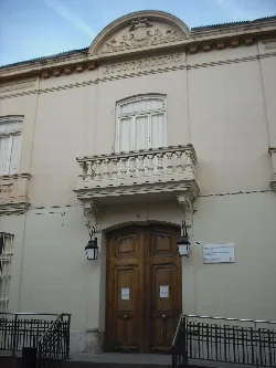 Edificio con fachada blanca y puerta de madera, con balcones y farolas.