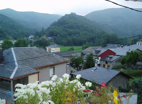 Häuser in Vega de Valcarce mit einer Burg auf dem Hügel im Hintergrund.