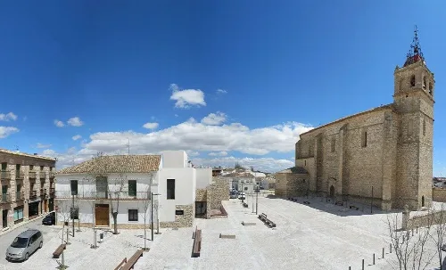 Platz des Cerrillo mit Bänken, Bäumen und einer alten Kirche in Horcajo de Santiago.
