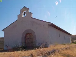 Small white chapel with bell tower and wooden door in a rural setting.