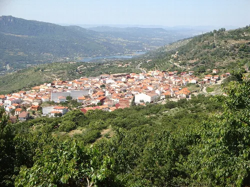 Panoramablick auf eine Stadt in einem Tal, umgeben von grünen Hügeln.