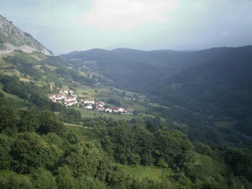Kleines Dorf mit weißen Häusern in einem Tal, umgeben von grünen Bergen.