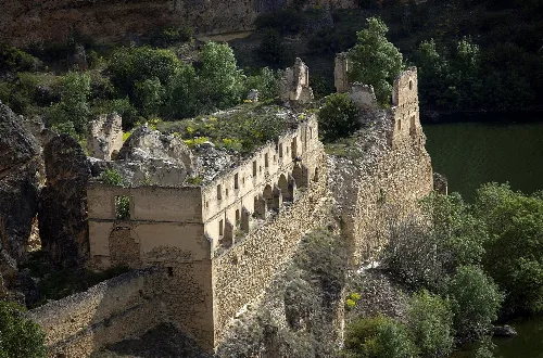 Ruins on a cliff with vegetation and river in the background.