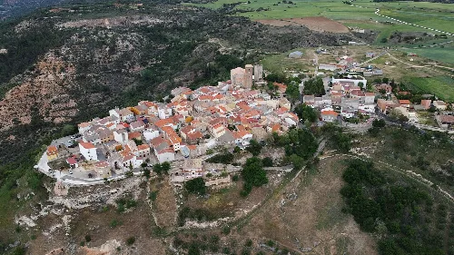 Luftaufnahme eines Dorfes mit Häusern und Straßen in einer hügeligen Landschaft.