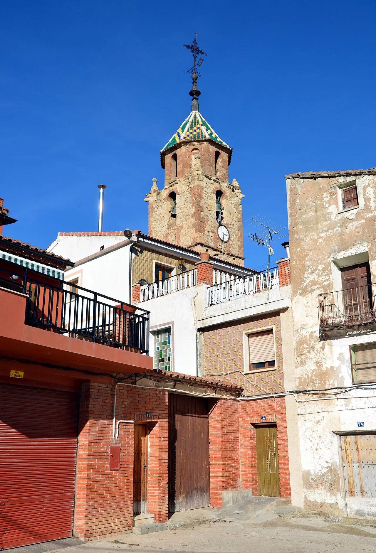 Glockenturm der Kirche in Tormón, Teruel, mit umliegenden Gebäuden und blauem Himmel.