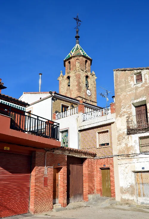 Glockenturm der Kirche in Tormón, Teruel, mit umliegenden Gebäuden und blauem Himmel.