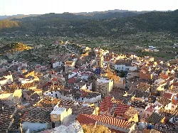 Vista aérea de un pueblo con calles estrechas, tejados rojos y montañas en el horizonte.