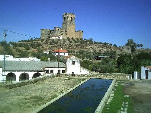 Burg auf einem Hügel mit einem Teich im Vordergrund und Häusern drumherum.