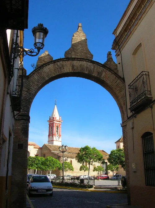 Arco de piedra en la calle con vista a la iglesia y su torre en el fondo