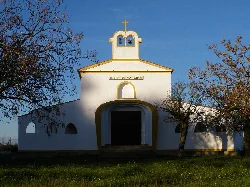 Small white hermitage with cross on top and trees around.