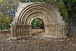 Steinbogen mit Inschriften und romanischer Verzierung in einem Park.