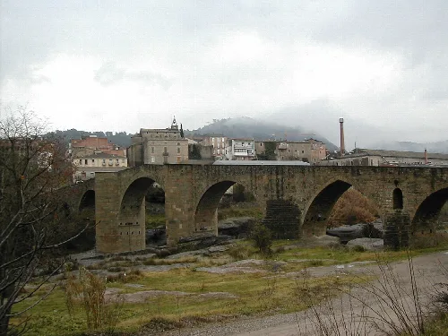 Steinbrücke mit Bögen und Gebäuden im Hintergrund an einem bewölkten Tag