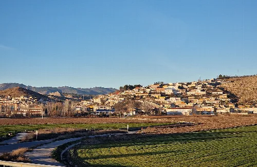 Landschaft von Pinos Puente mit Häusern am Hang und Feldern im Vordergrund.