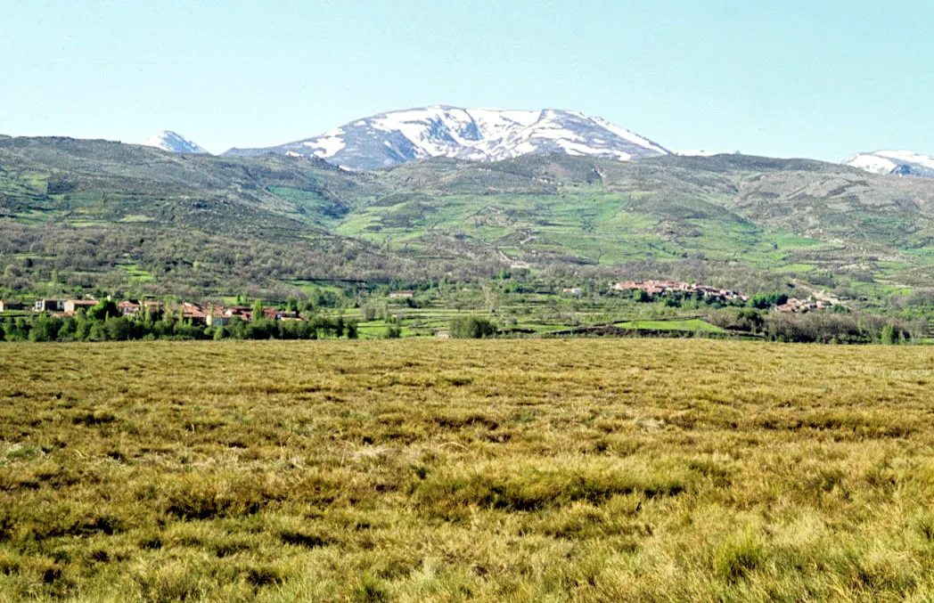 Landscape with snow-capped mountains, green fields, and small villages in Ávila.