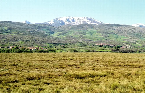 Landschaft mit schneebedeckten Bergen, grünen Feldern und kleinen Dörfern in Ávila.