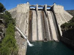 Large concrete dam with water at the base and vegetation on the sides.