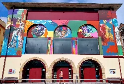 Facade of the theater with a colorful mural and three arches at the entrance.