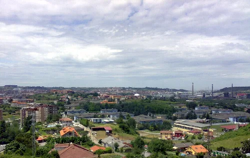 Vista de Avilés con edificios y áreas verdes bajo cielo nublado.