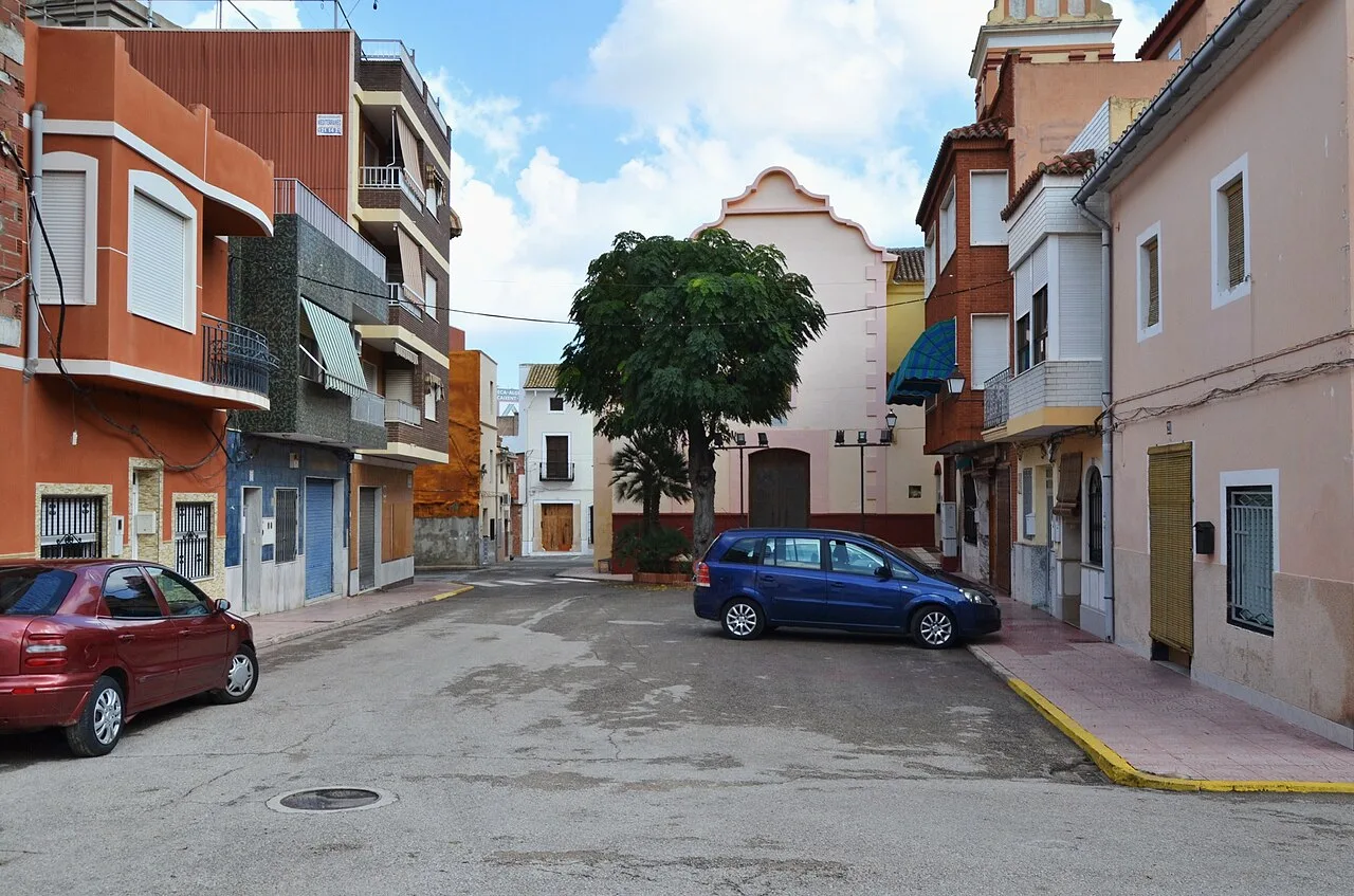 Square with trees, residential buildings, and two parked cars.